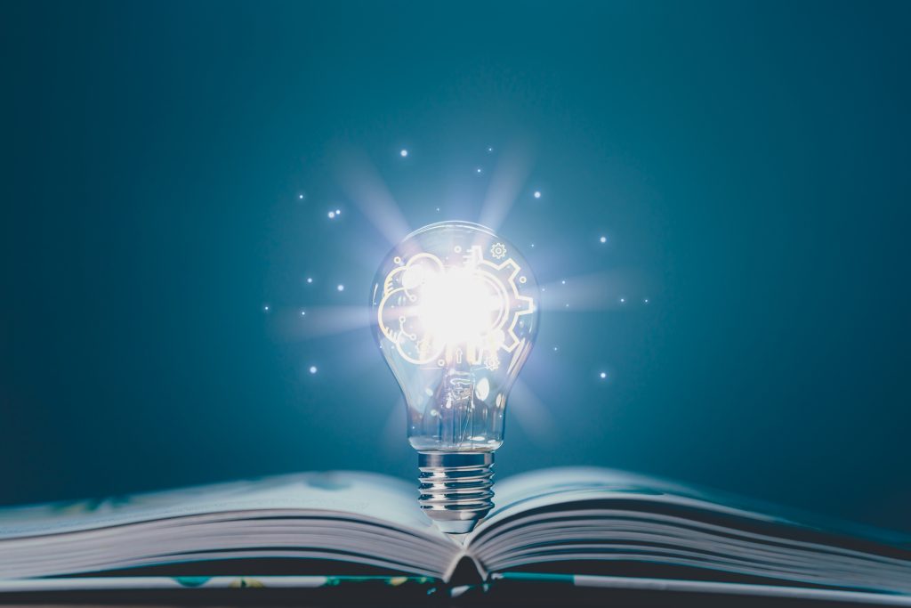Book laying on a table, opened with a Glowing light bulb twinkling with lights