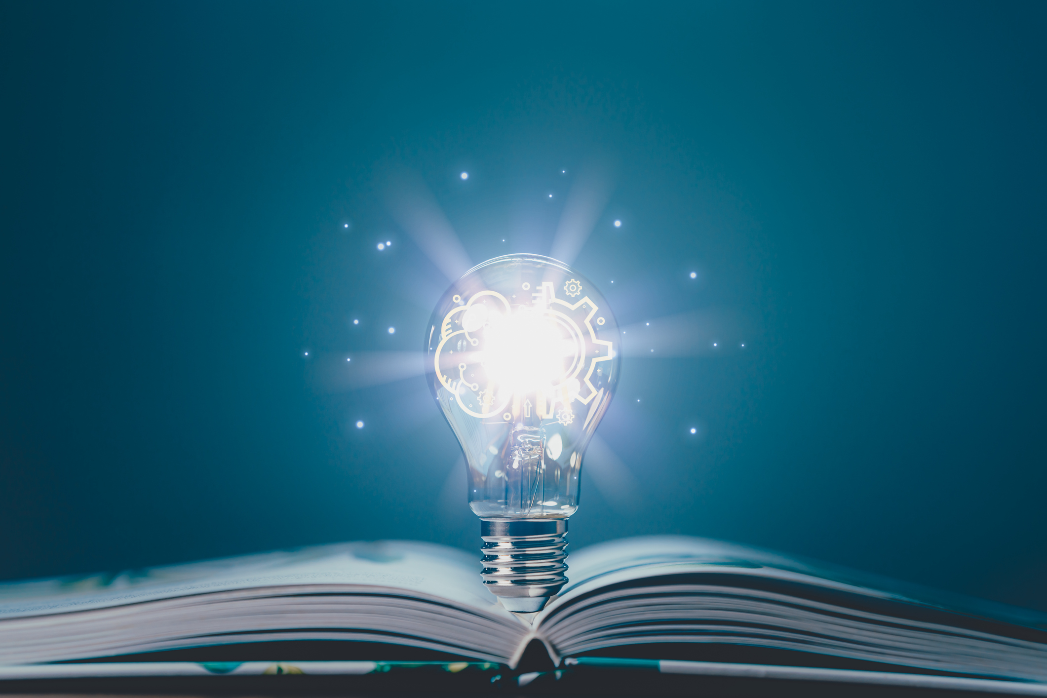 Book laying on a table, opened with a Glowing light bulb twinkling with lights