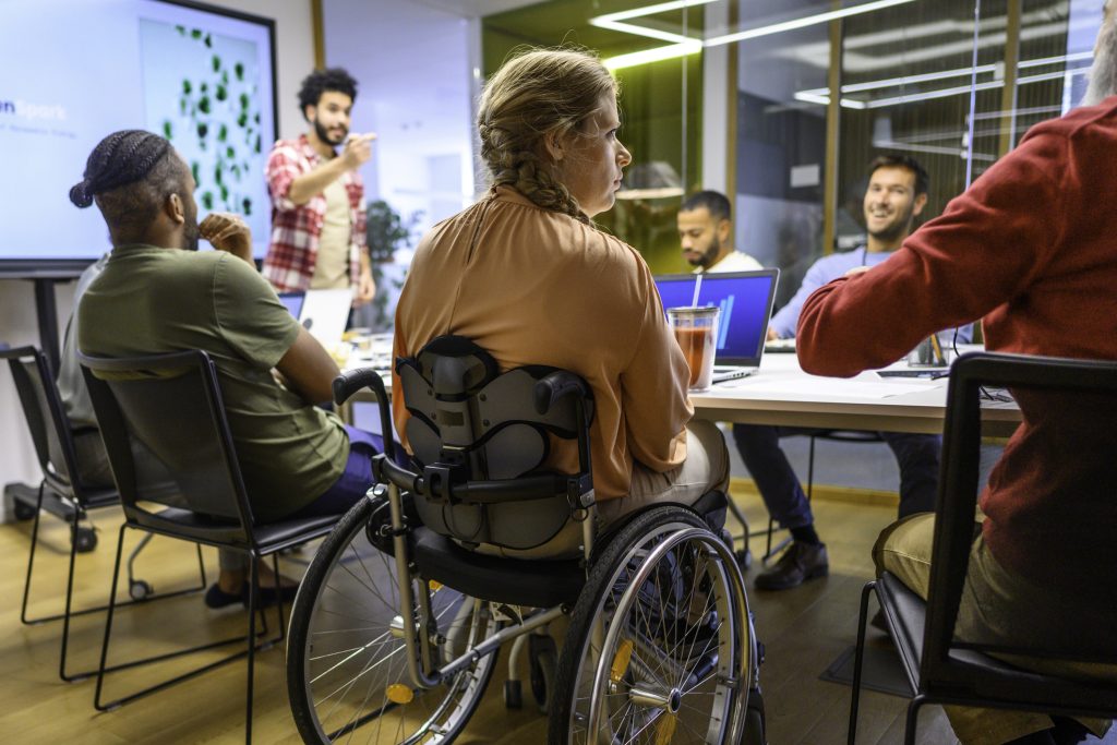Conference room with multiple people sitting at the table, with one of them being in a wheel chair