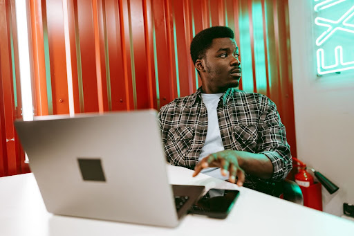Man sitting at a table with a laptop and his phone on the table in front of him.